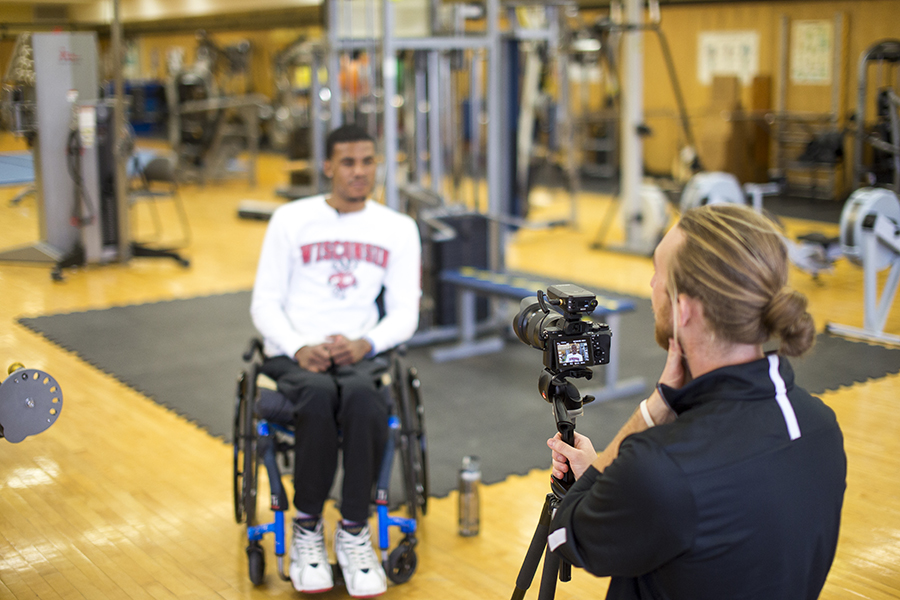 Photo of a man in a wheelchair having his photo taken in an indoor gym