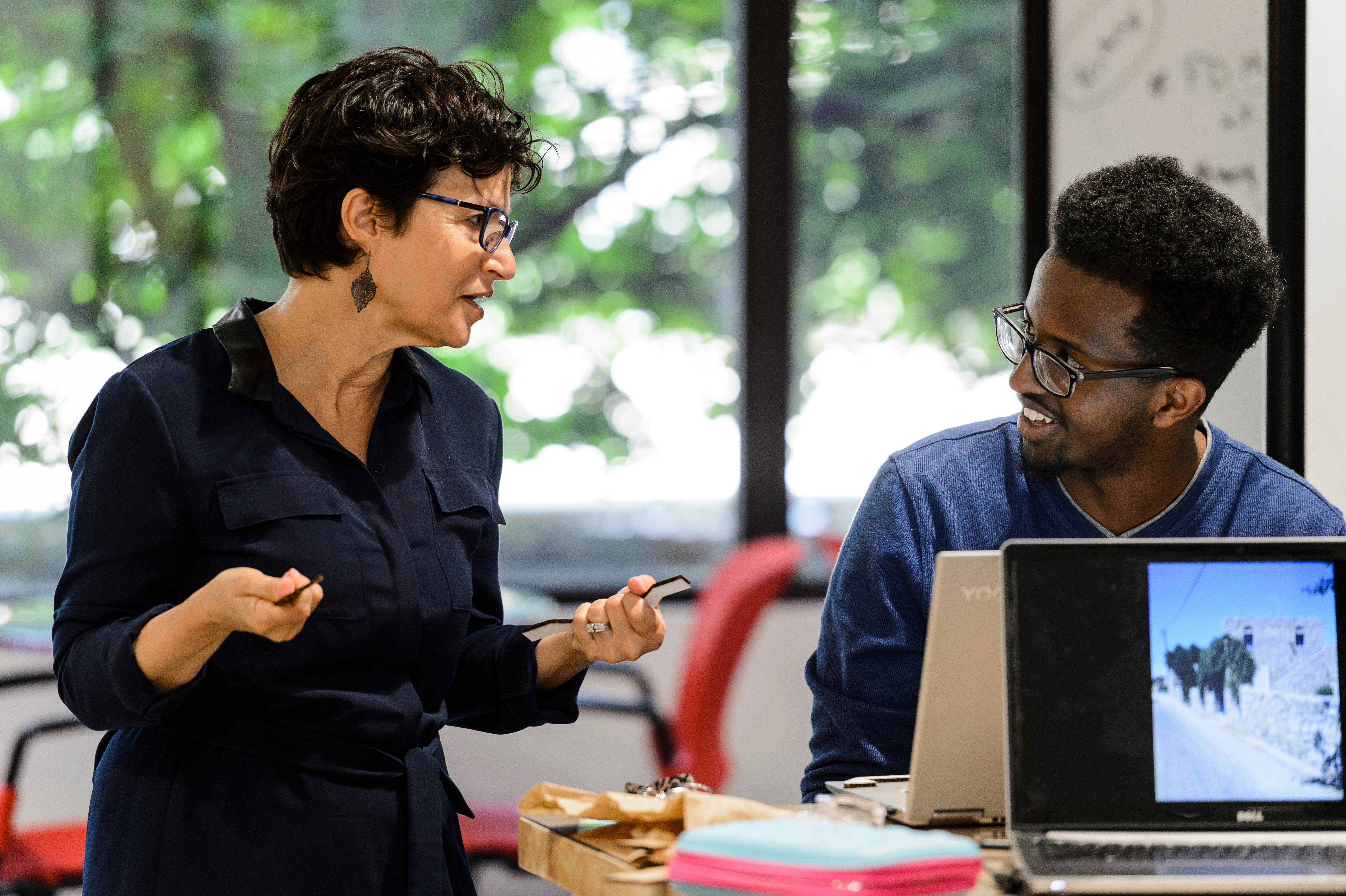 Photo of a man and a woman talking to each other as the man works on a laptop