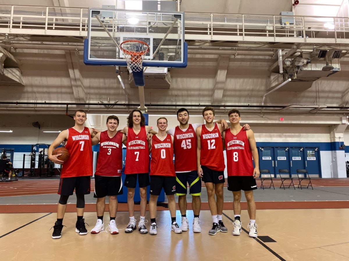 A photo of 7 players of the Men's Club Basketball team in front of a hoop at the Camp Randall Sports Center