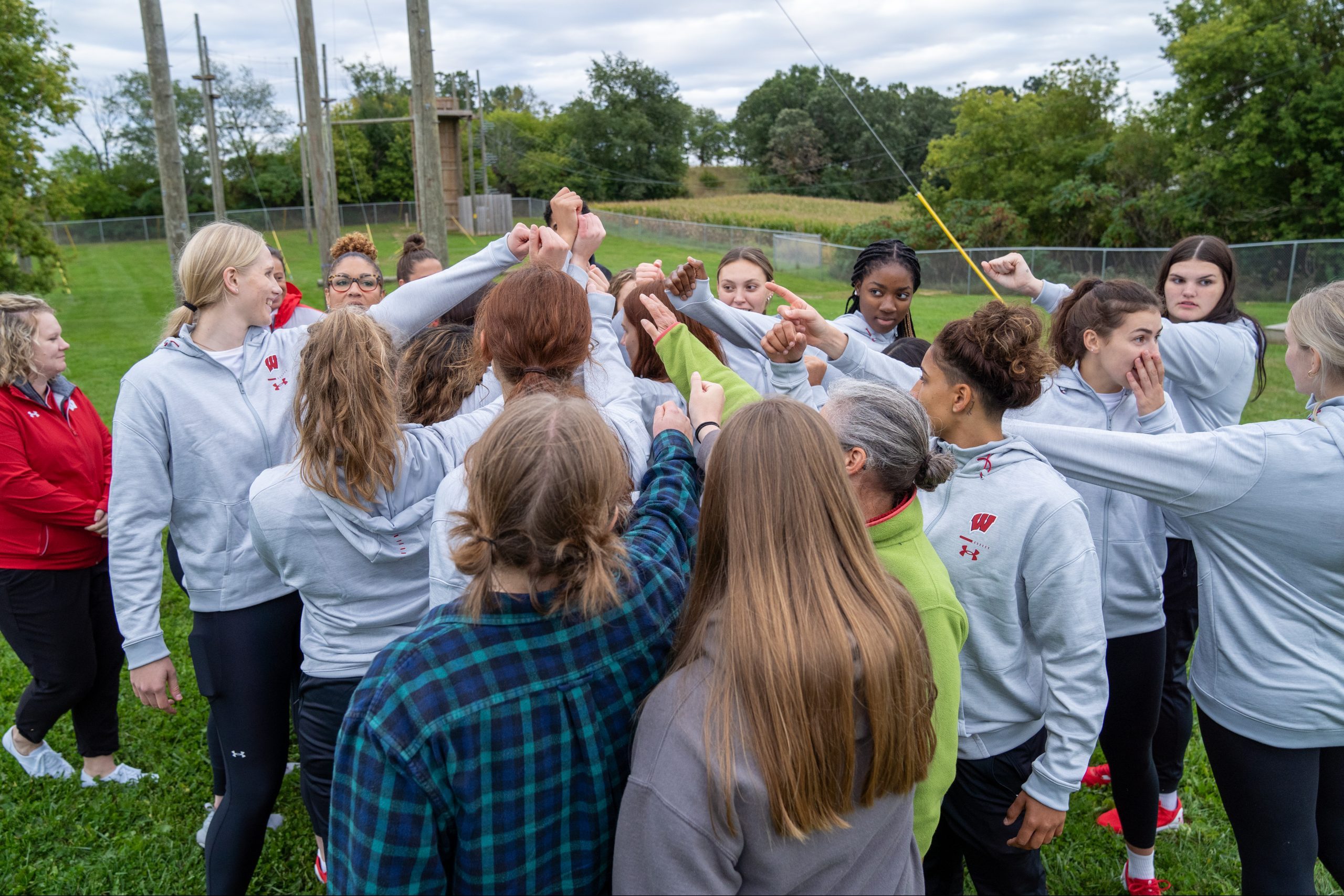 Students stand in a circle with their hands together in a show of teamwork.