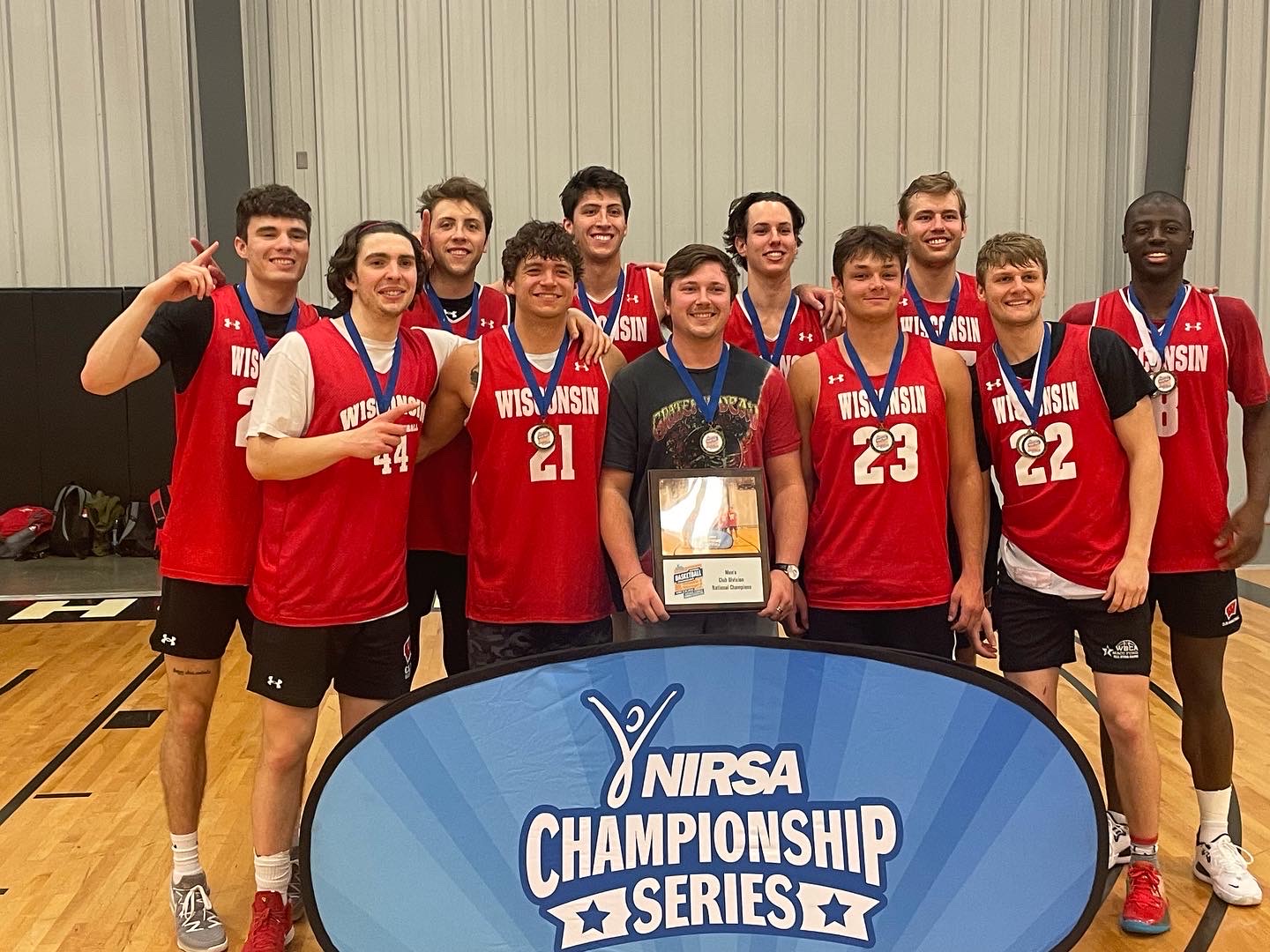Photo of the UW Men's Basketball Club standing together with medals holding a bracket in an indoor gym