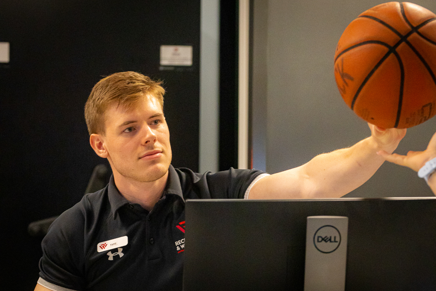 A photo of a student employee handing a basketball to another student.