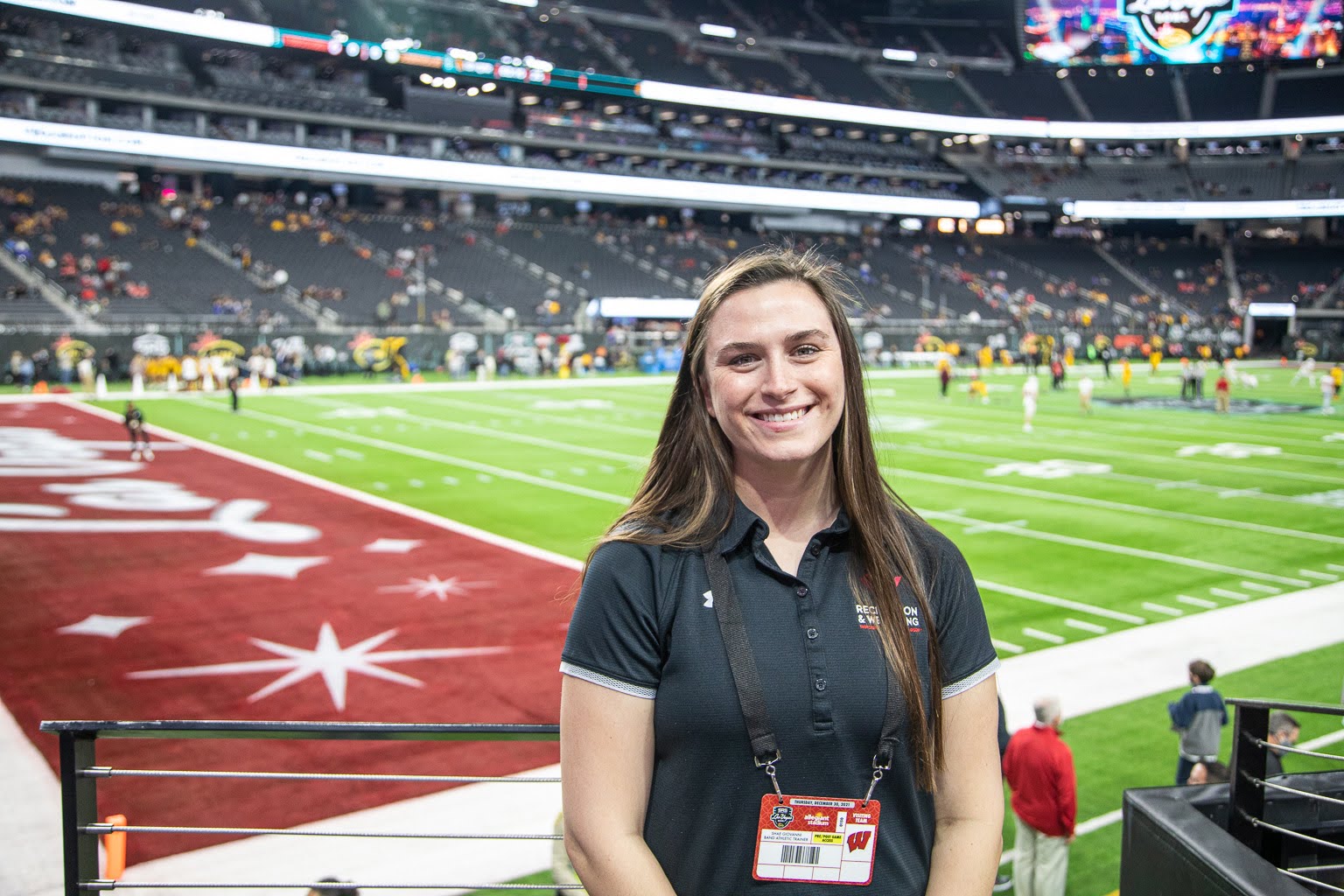 Shea, an athletic trainer, standing on the sidelines of a football field.