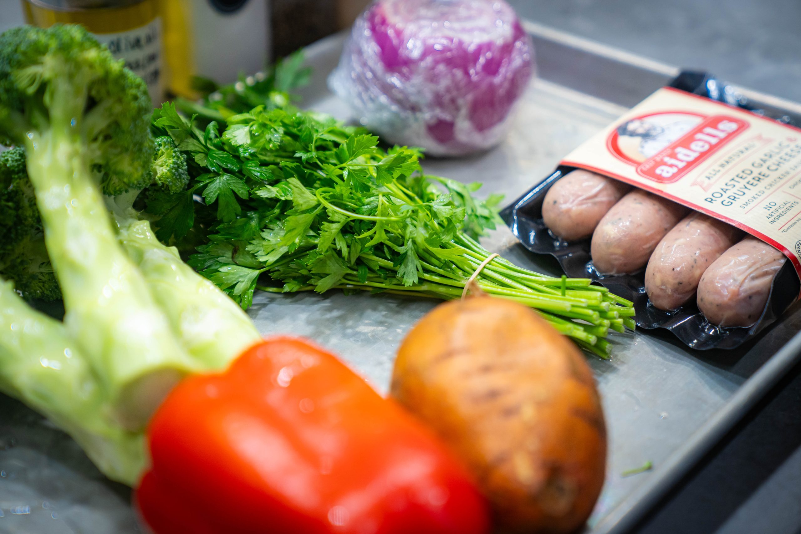 Various ingredients such as broccoli, red pepper, potato, cilantro, onion, and sausages
