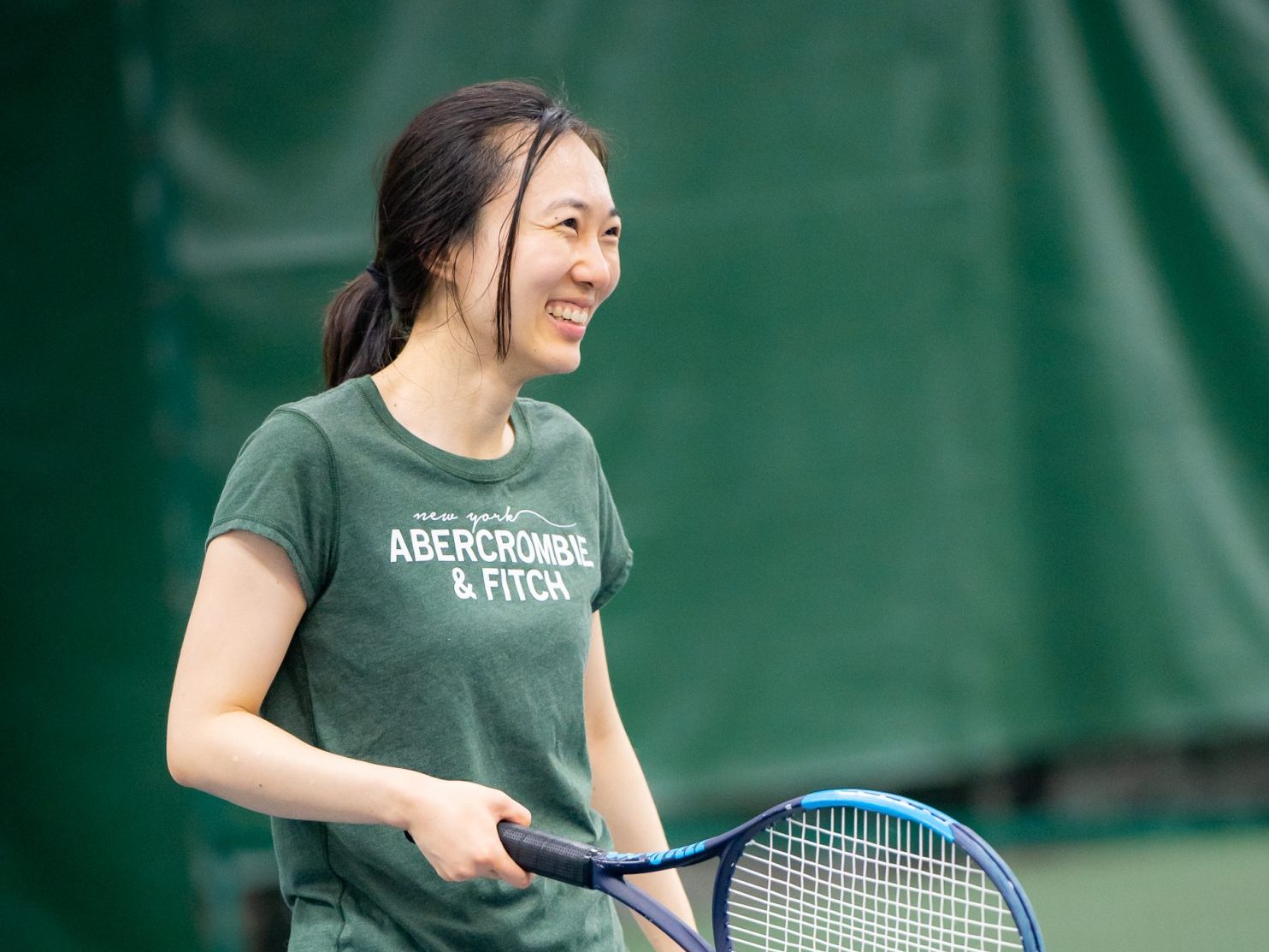 Image of student smiling and holding a tennis racket at the Nielsen Tennis Stadium