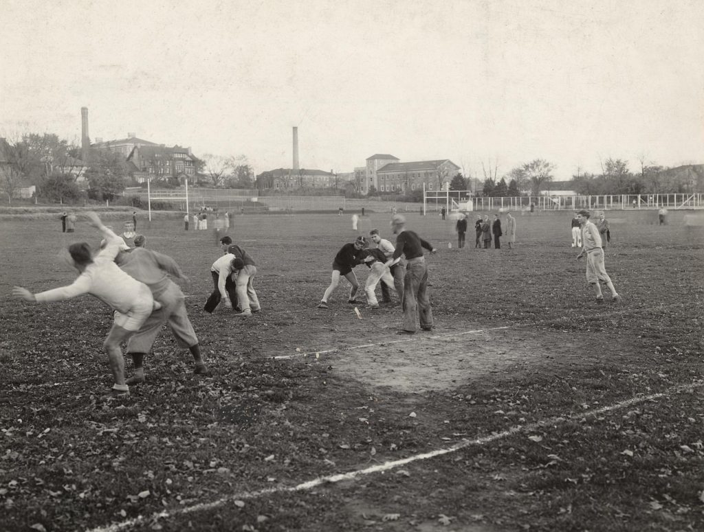 Students practice football maneuvers on playing fields near Agriculture buildings.