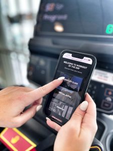 A photo showing a close-up of a phone who has scanned the QR code "Workout of the Day" sticker on a cardio machine. The image shows a person's hand selecting the workout. 