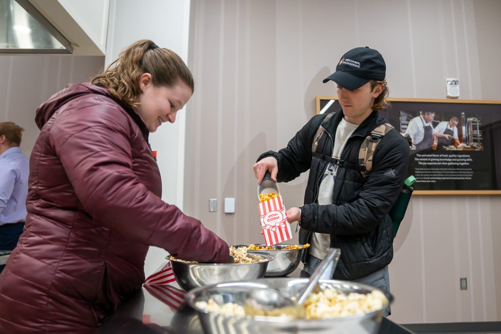 A photo of two students scooping popcorn into bags.