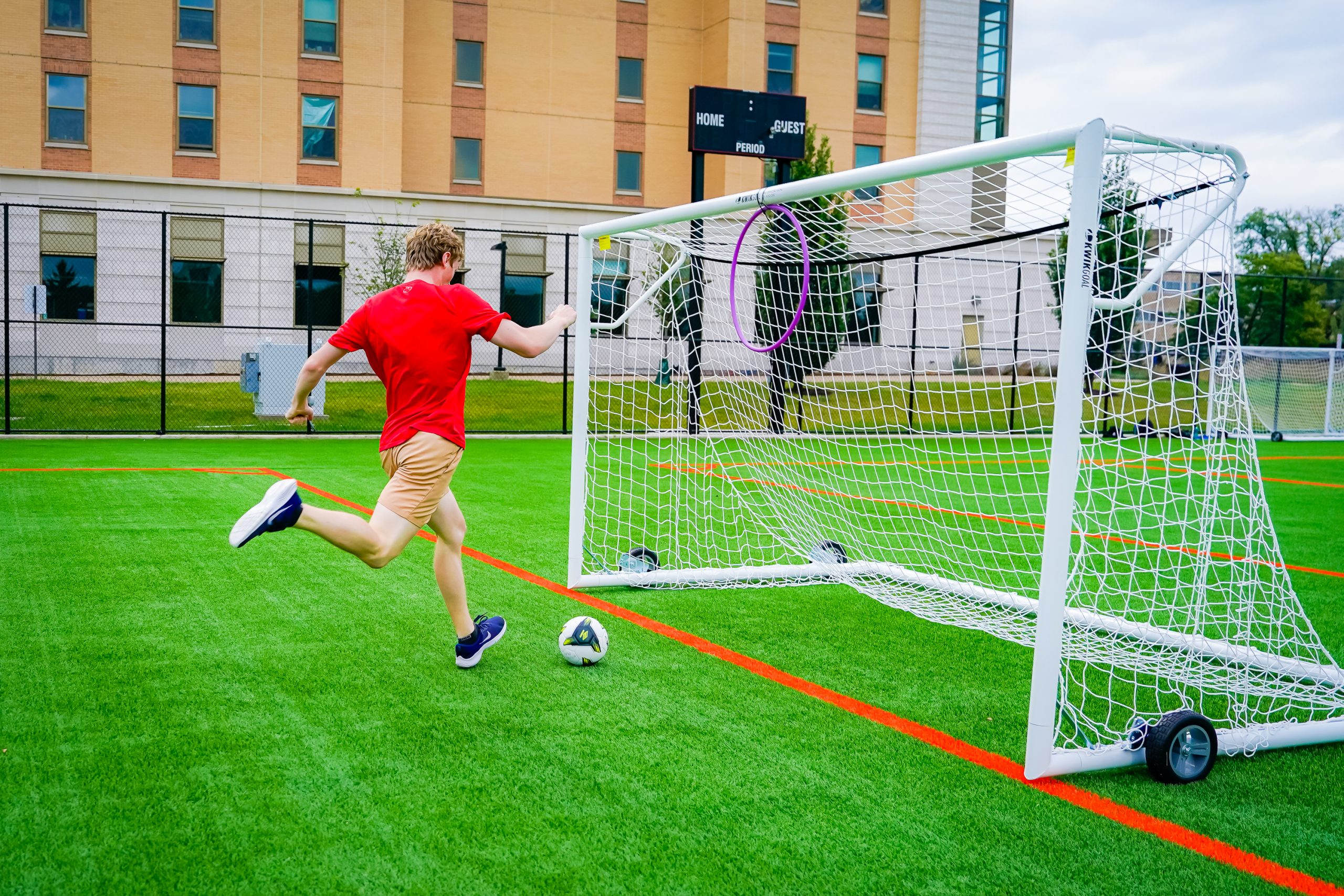 A person in a red shirt kicks a soccer ball into a goal. 