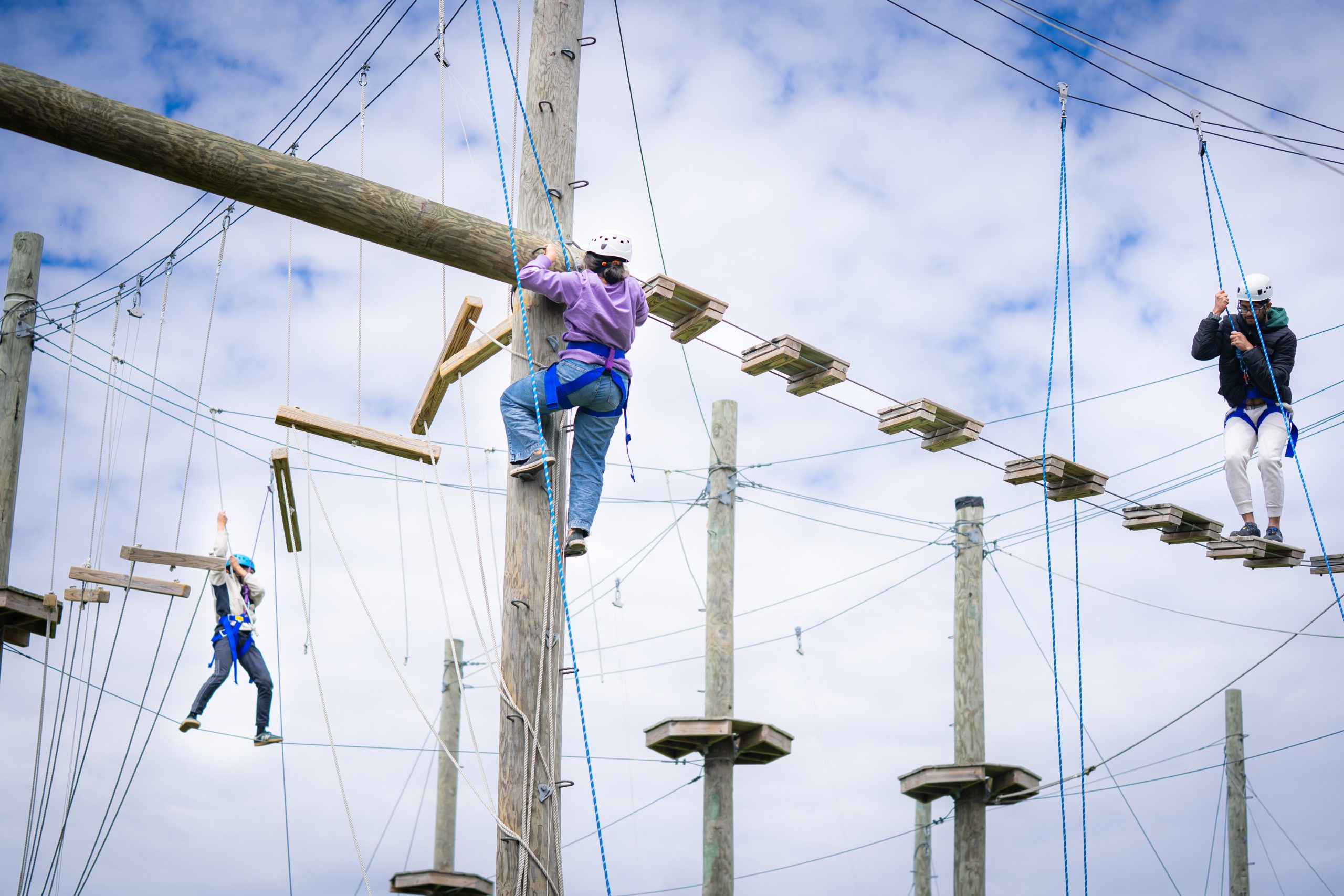 Three adults wearing climbing gear participate in the ropes course. 