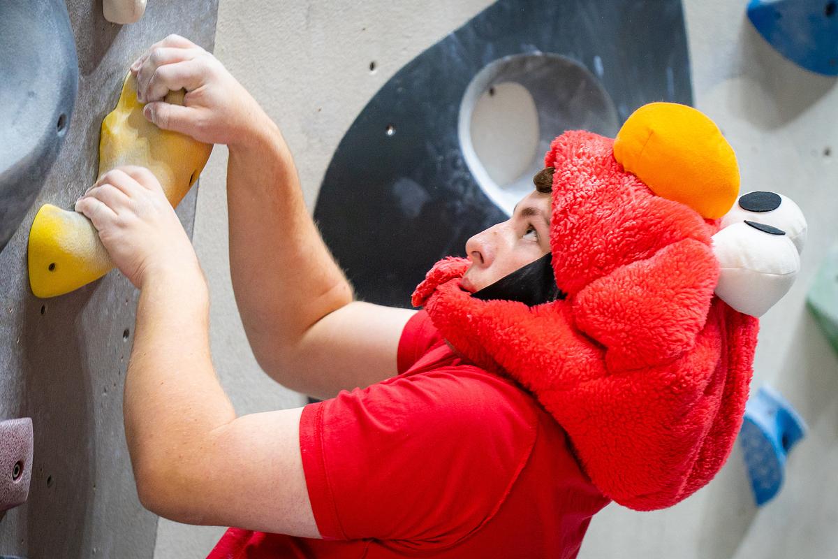 A photo of a climber ascending the climbing wall wearing an Elmo costume.