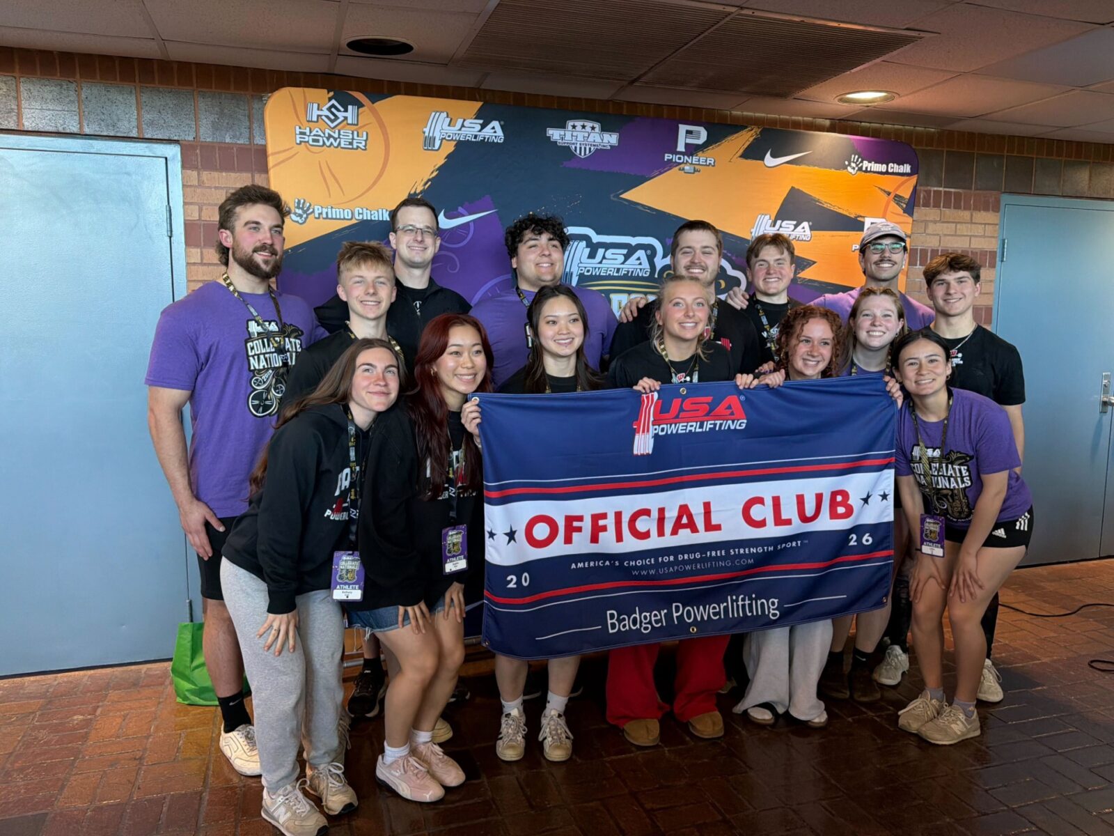 Students and coaches stand in front of a USA Powerlifting backdrop holding a banner.