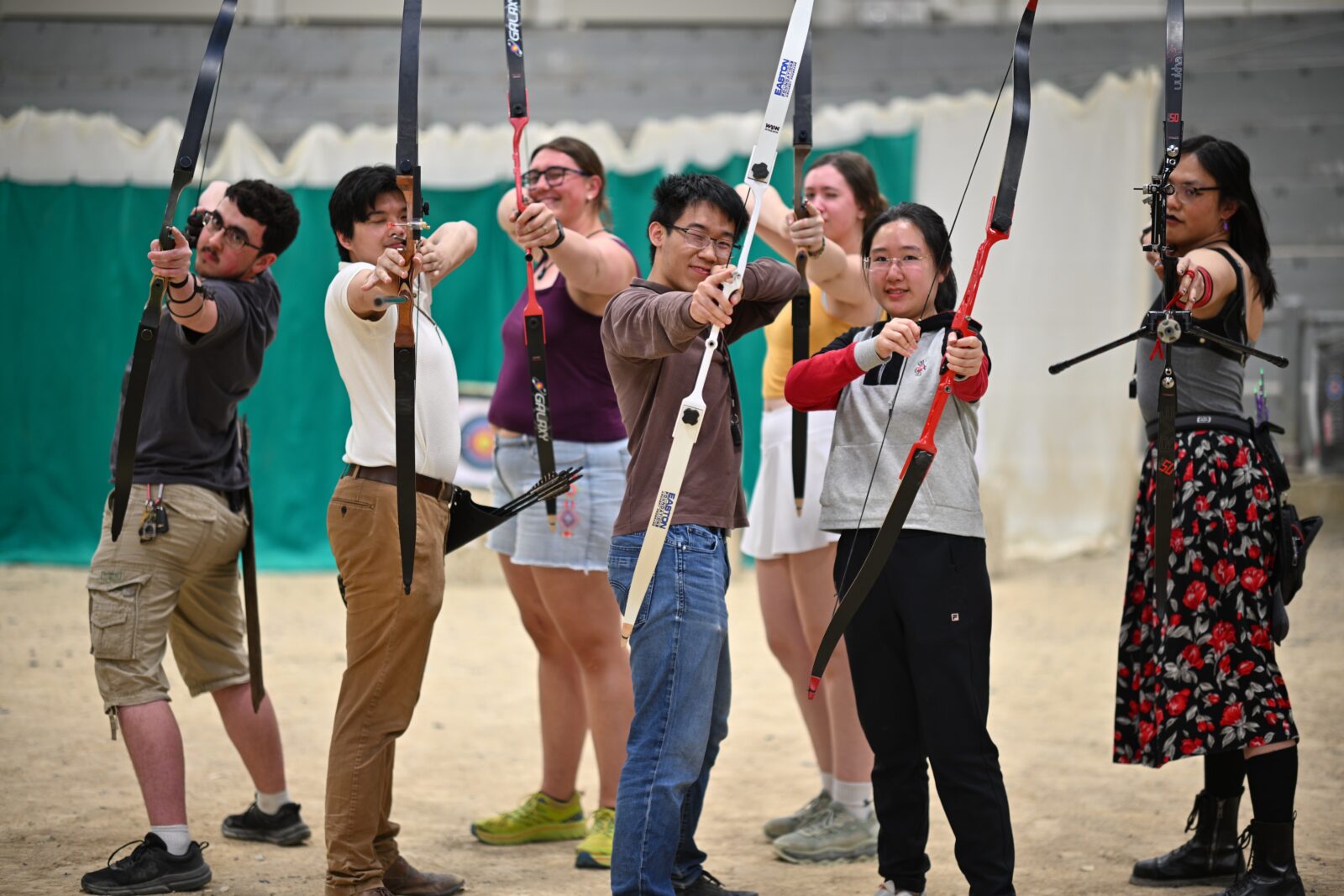 A group of students aims and draws their bows towards the camera.